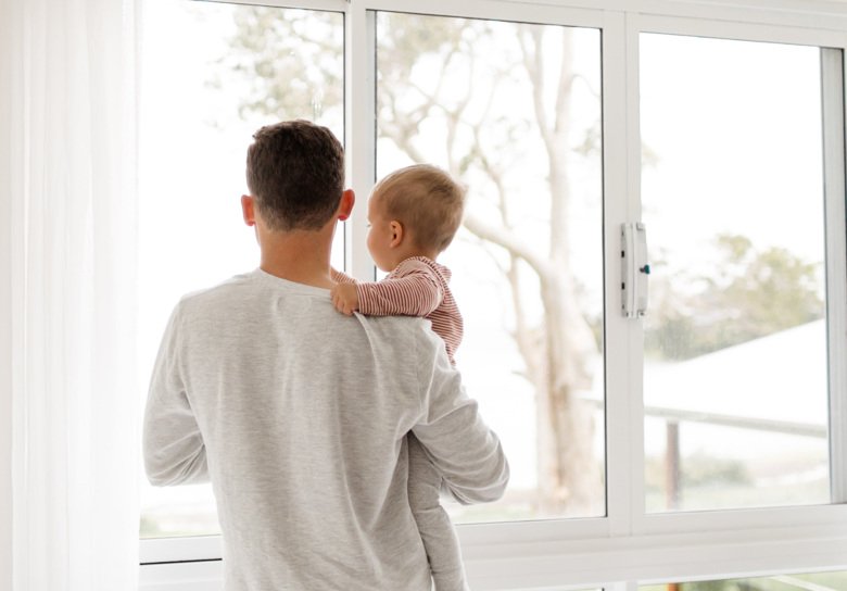 Pappa som håller ett barn i famnen och tittar ut genom fönster