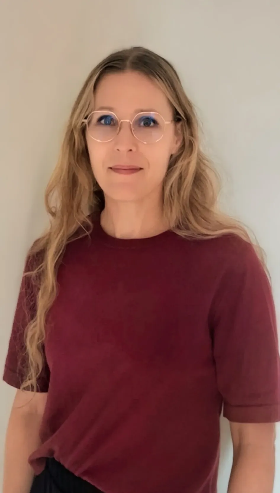 Profilbild på en kvinna med långt blont hår, glasögon och en vinröd topp