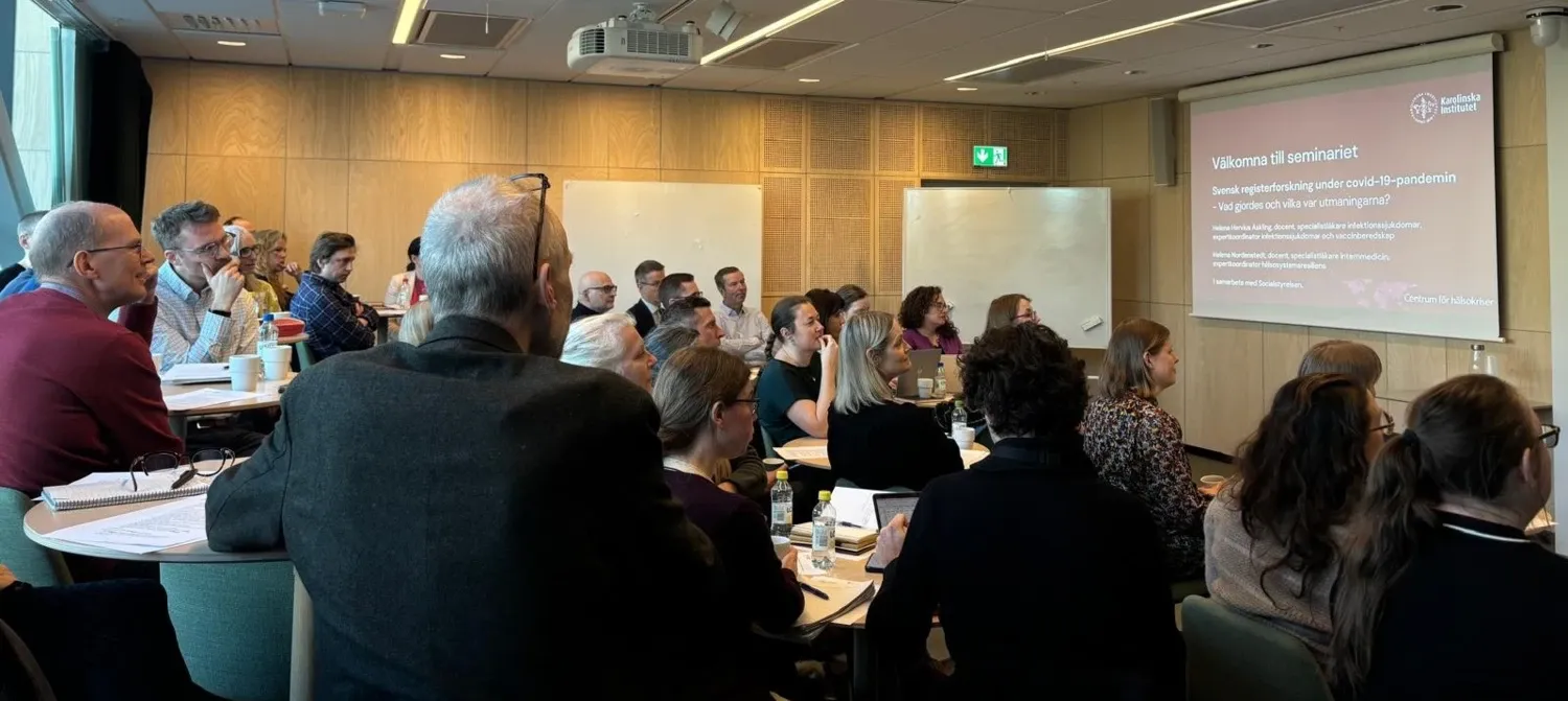 Personer sitter i publiken på ett seminarium och tittar upp mot en bildskärm där det står Centrum för hälsokriser