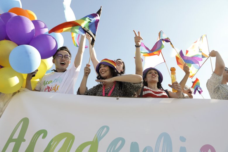 Studenter och personal viftar med flaggor i Pride-paranden genom Stockholms gator.
