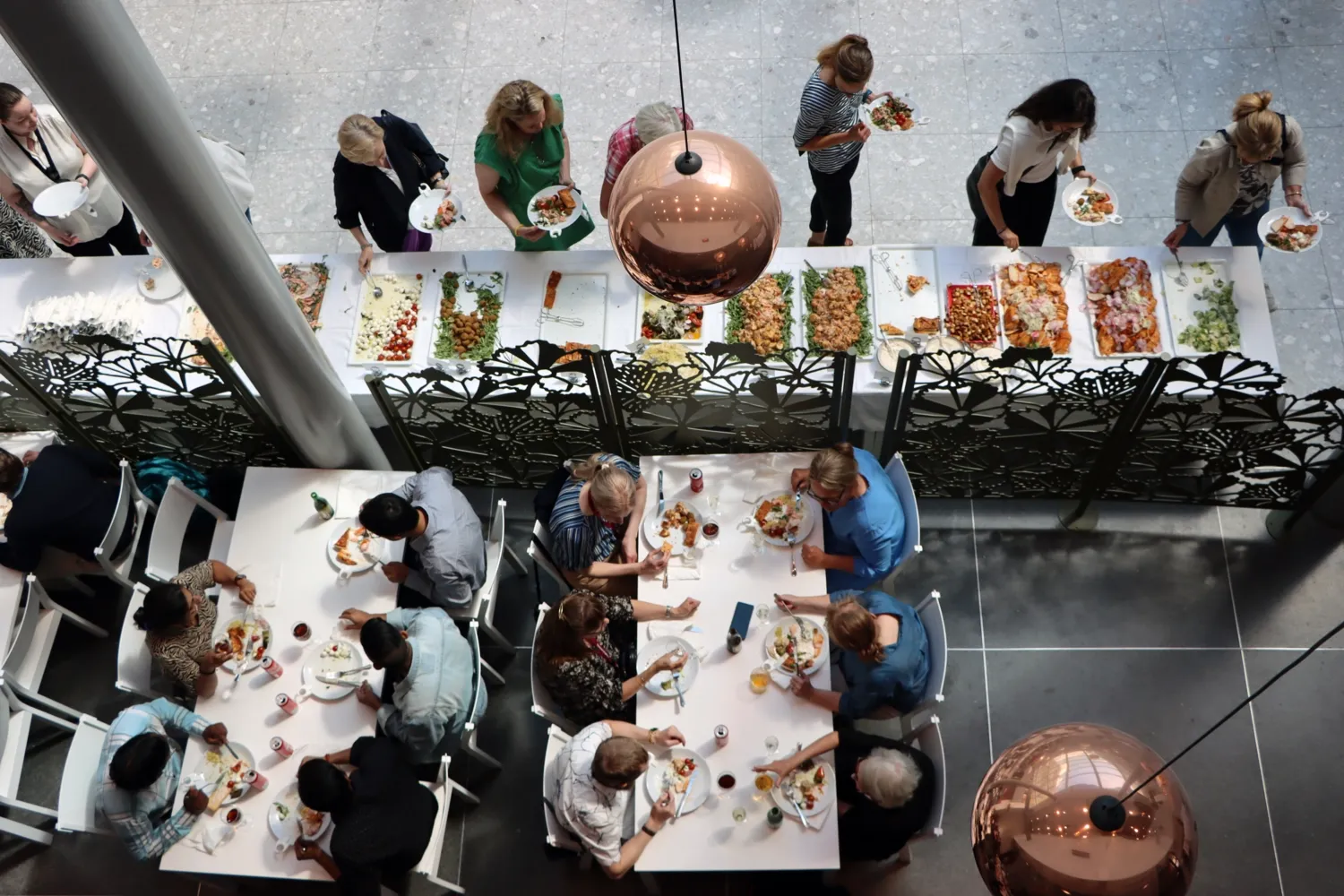 NVS sommarlunch 2024. Folk går och tar mat samt sitter till bords. Bilden tagen uppifrån.