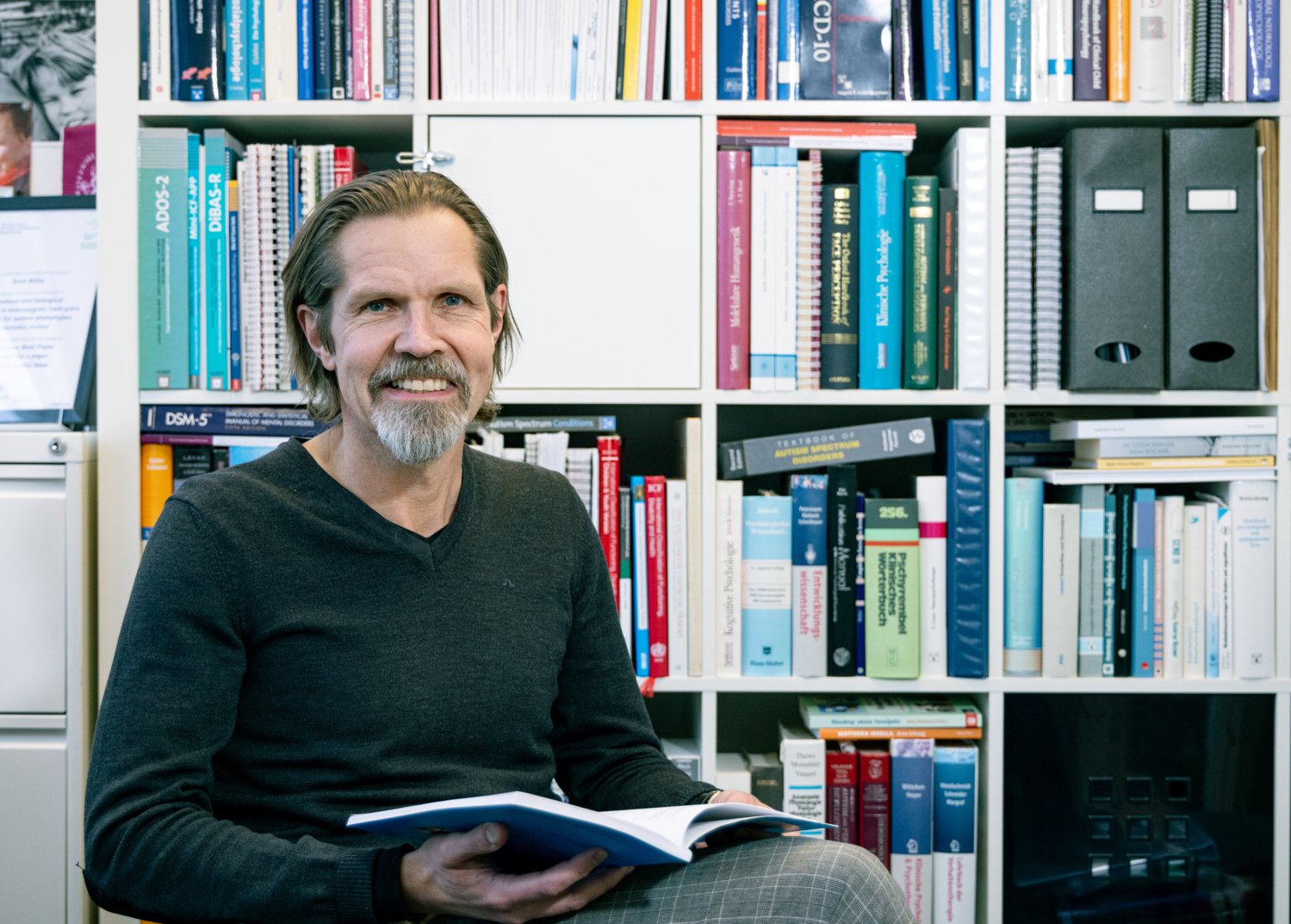 Man som sitter framför en bokhylla, tittar mot kameran och ler.