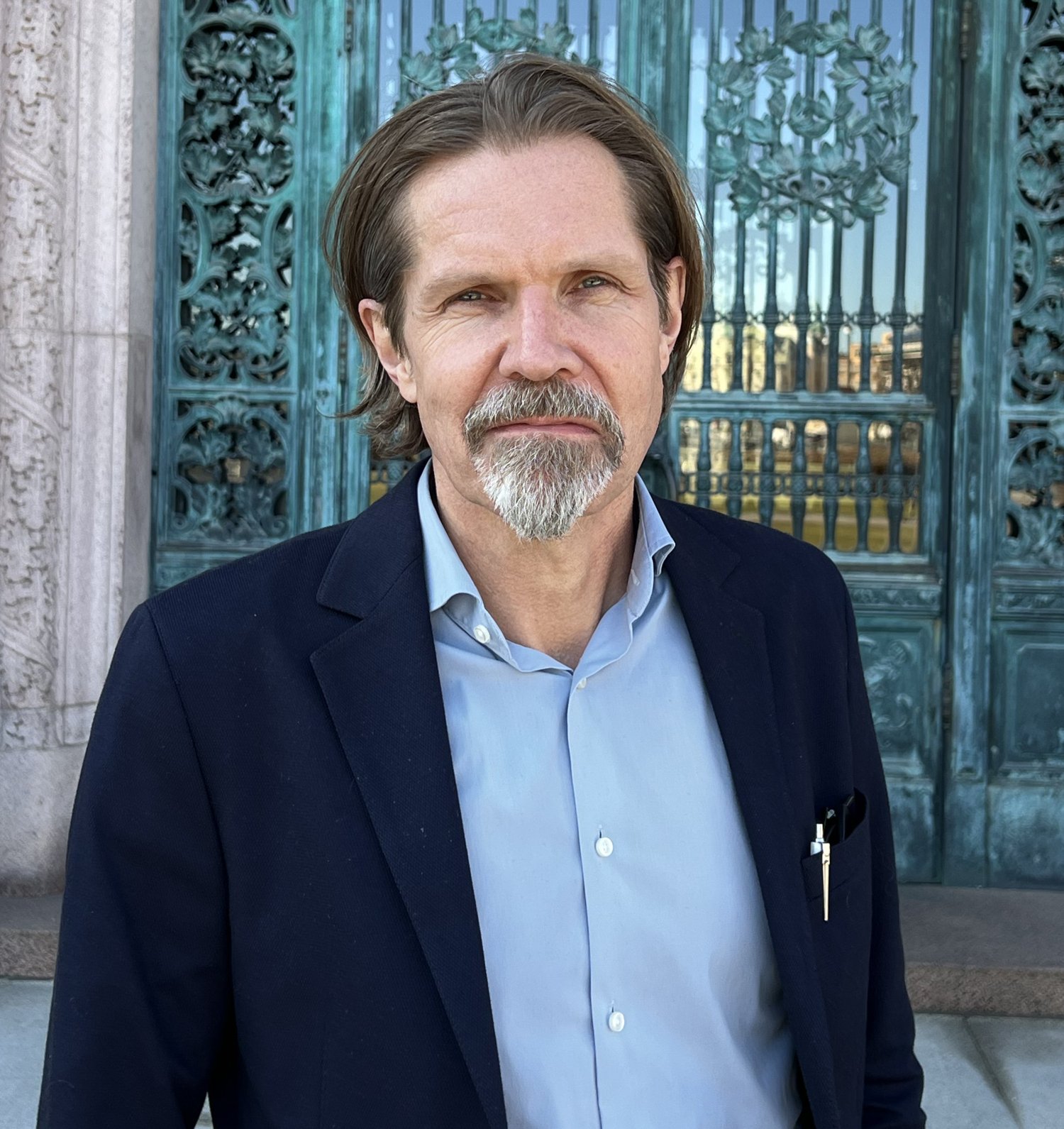 Man i kavaj framför en utsmyckad port.