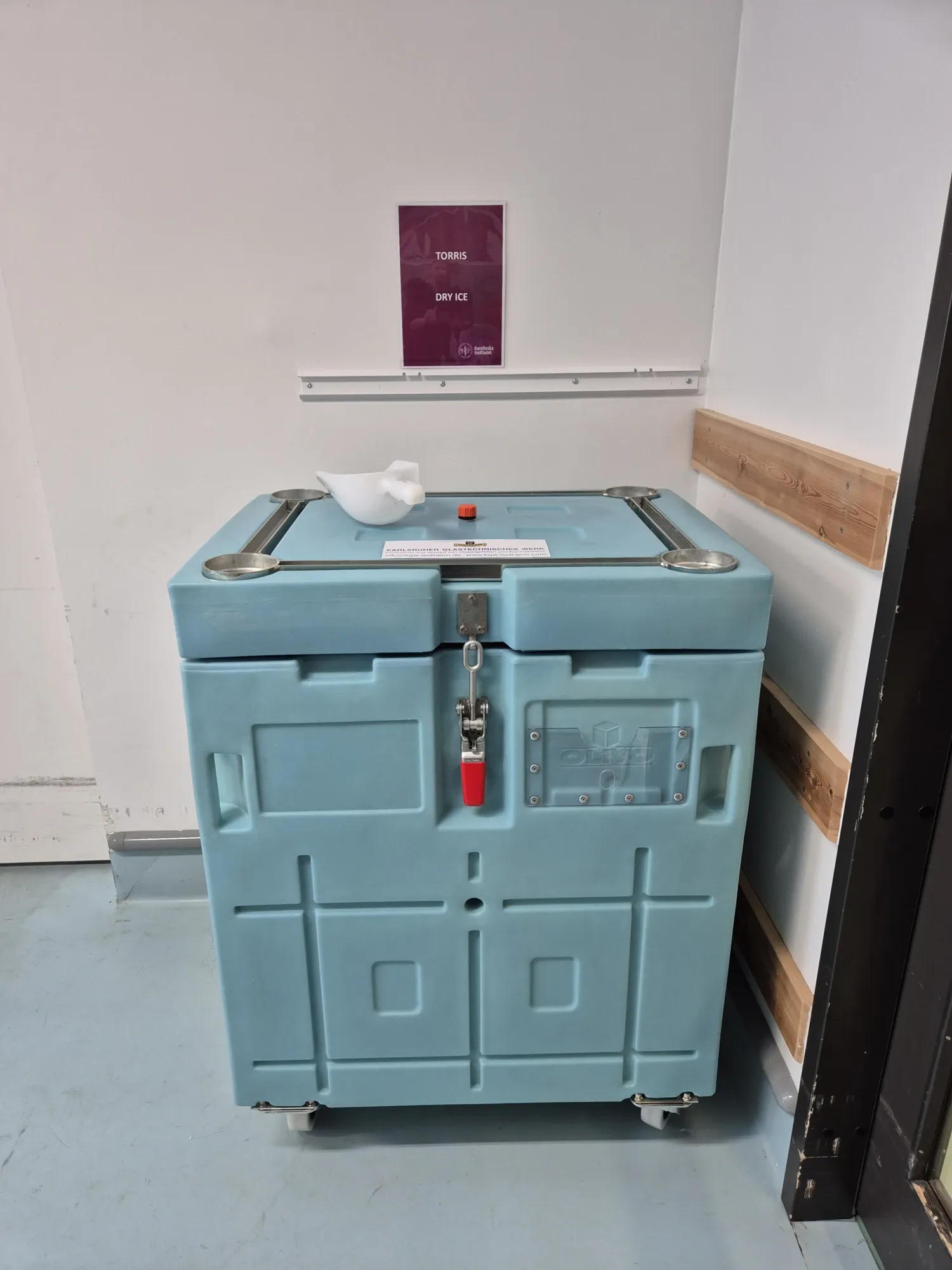 Foto av en turkos torris-box på hjul ståendes i ett rum.