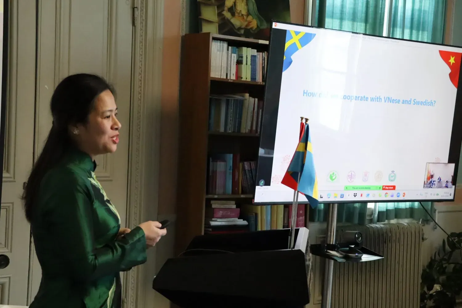 Hien Vu i traditionell grön vietnamesisk klänning presenterar framför skärm.