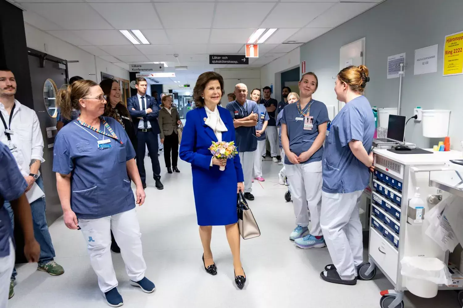 Drottning Silvia på rundvandring i sjukhuset. Gåendes i sjukshuskorridoren omgiven av medarbetare från sjukhuset.