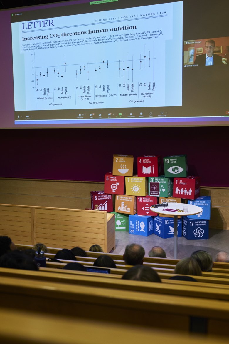 Bild på scenen med FN:s globala mål uppsatta i kuber. En digital presentatör visar power point med rubrik "Increasing CO2 threatens human nutrition".