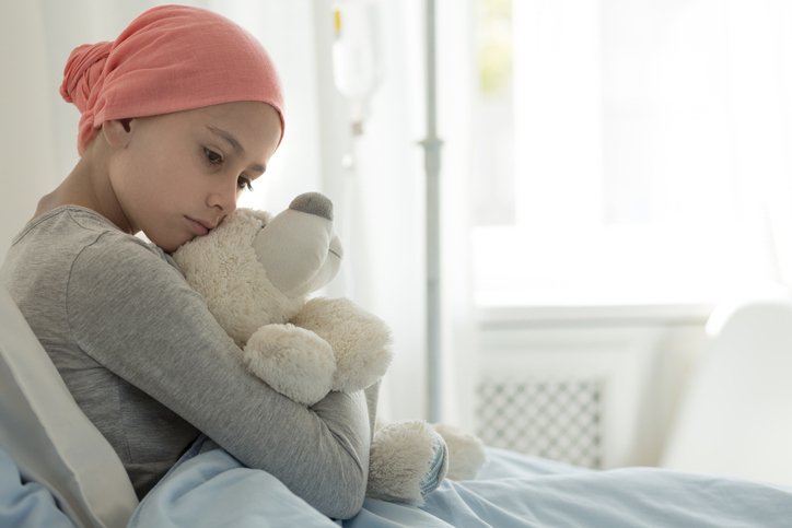 A child with cancer is sitting on a hospital bed
