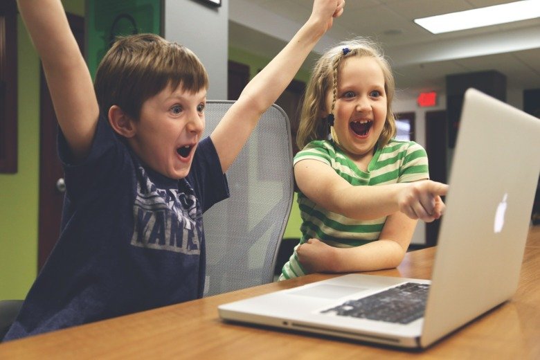 Två glada, uppspelta barn vid en dator