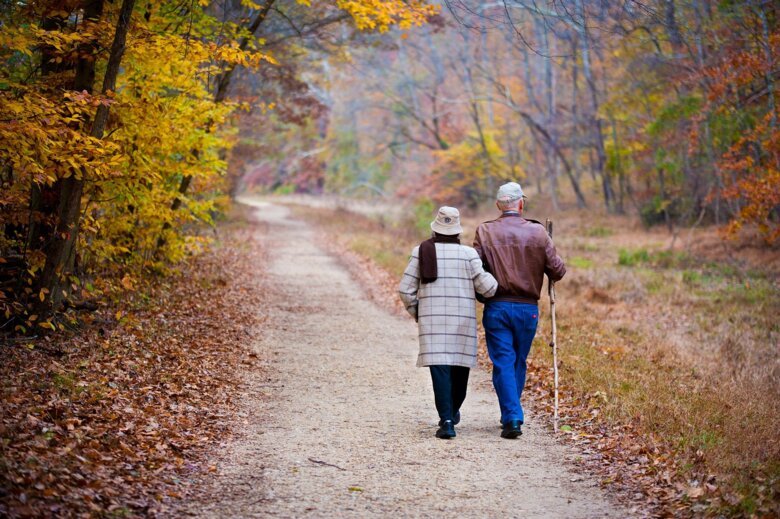 Par som går på skogsväg omgärdad av höstfärgade lövträd