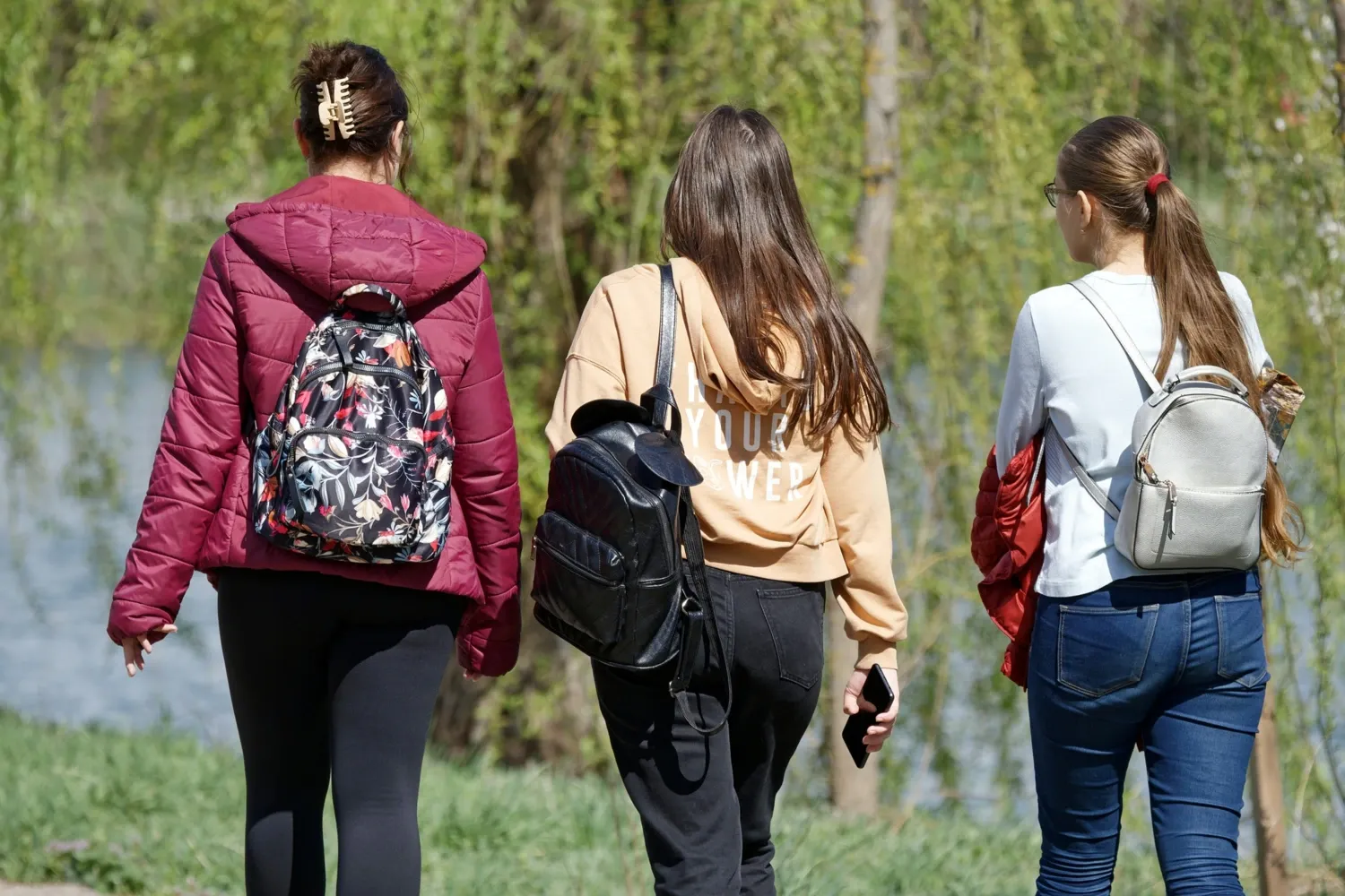 Tre tjejer som går med ryggsäckar mot grön bakgrund