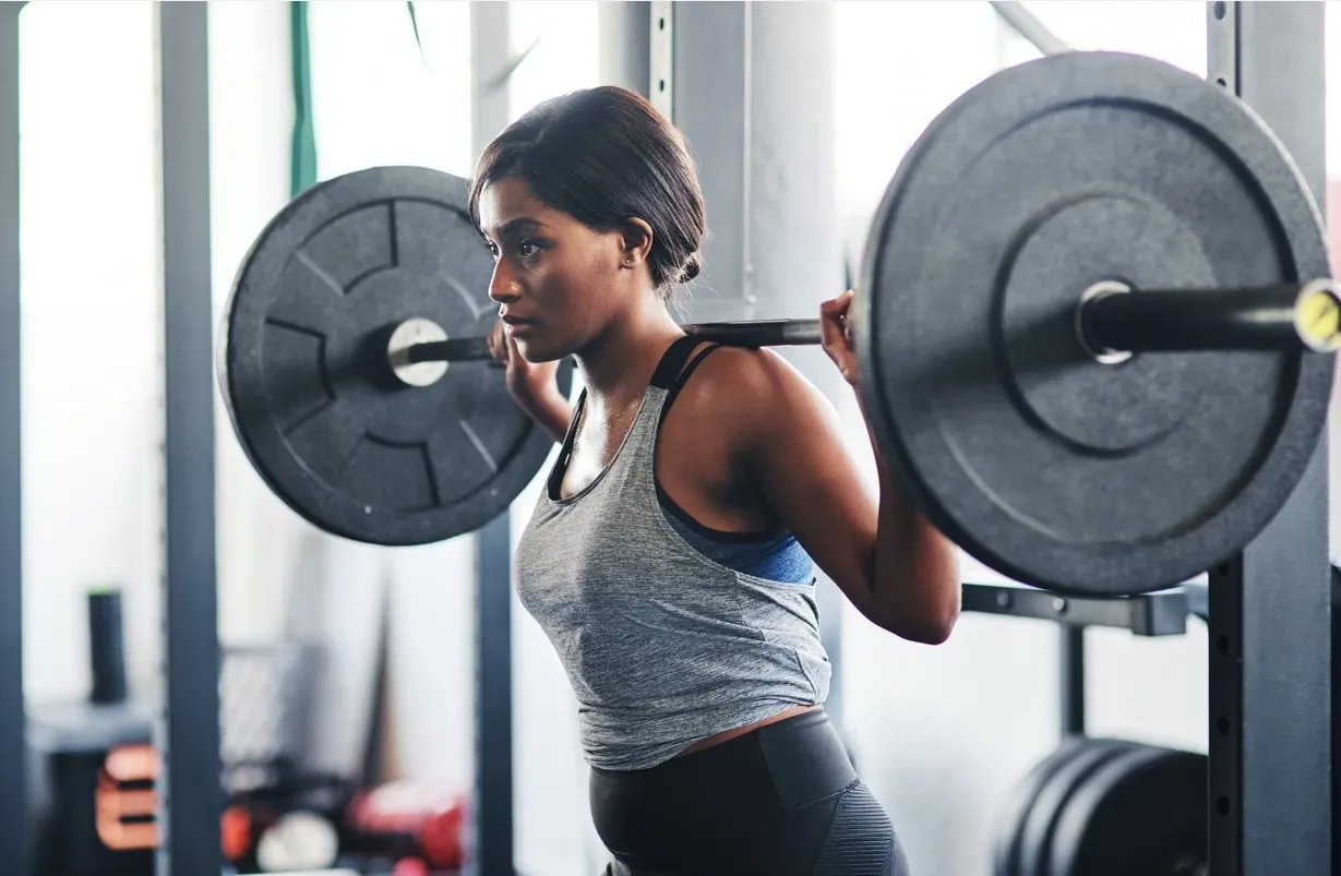 Mörk kvinna med skivstång på axlarna