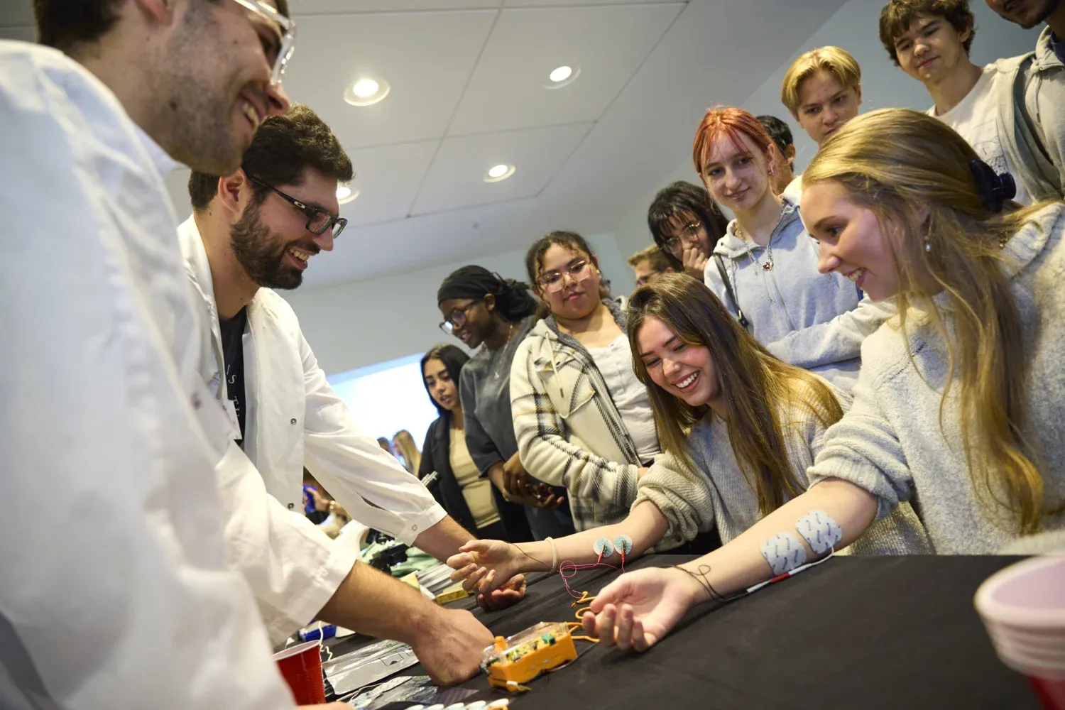 Två gymnasietjejer sitter vid ett bord med sladdar på armarna.