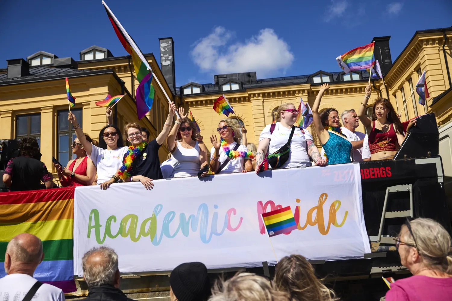 Grupp personer på flak med texten academic pride på viftar med regnbågsflaggor.