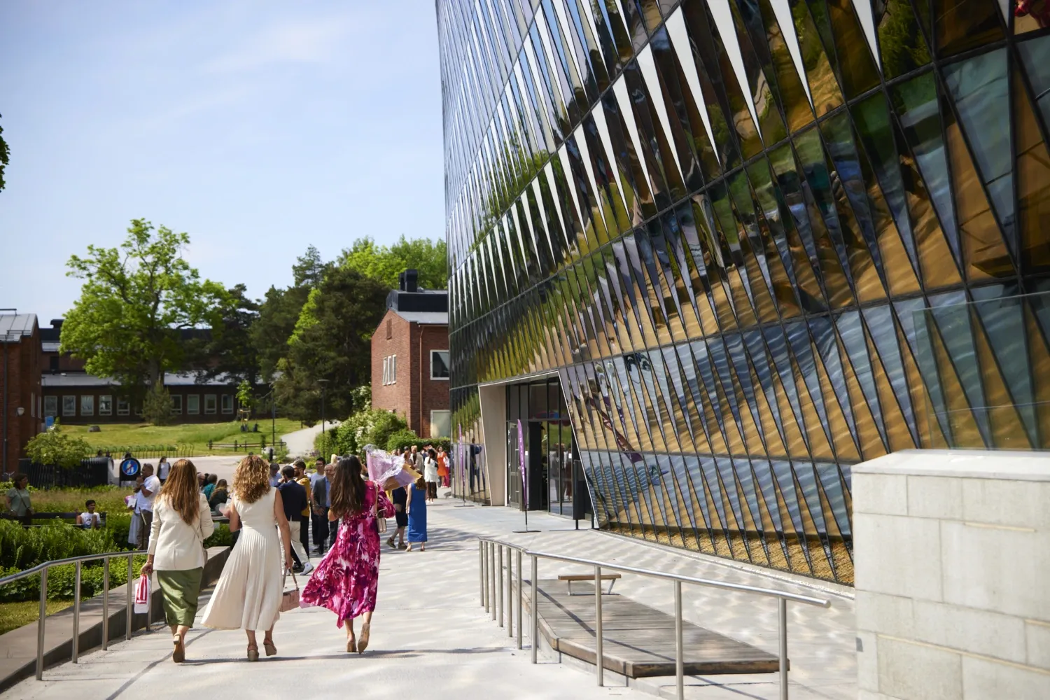 Färgglatt klädda studenter går bredvid Aula Medica under en klarblå himmel.