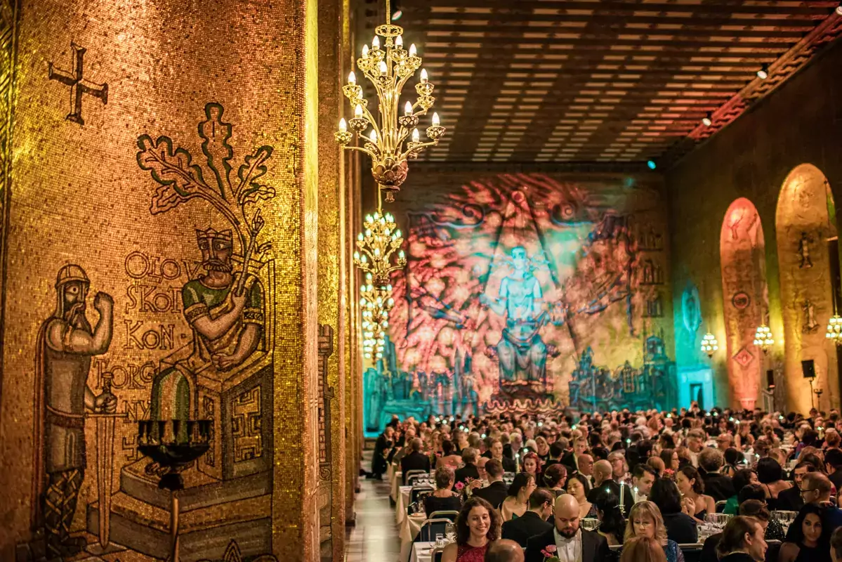 Konstverk på väggen av gyllene salen med sittande bankettgäster i bakgrunden.