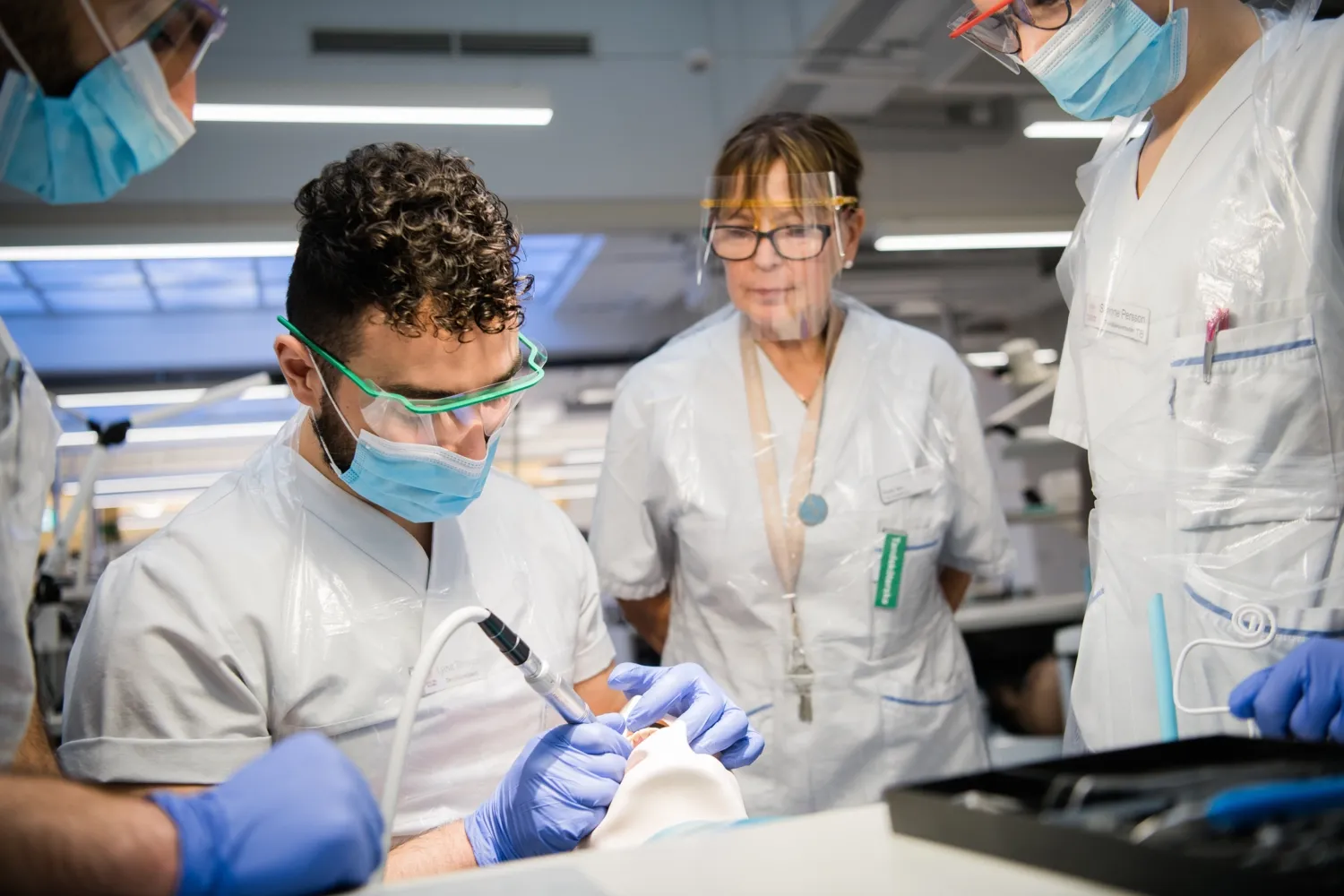 Dental student examining a dummy, supervisors in the background.