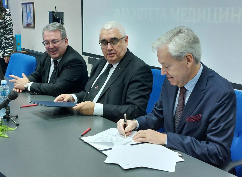 Tre män vid skrivbord som undertecknar en överenskommelse
