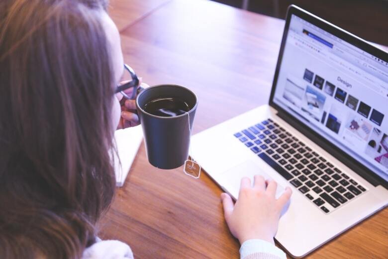 Person holding a tea mug while using a laptop.