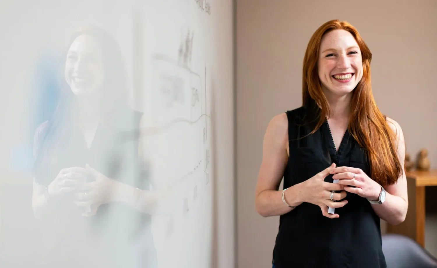 Bild på en kvinna med långt rött hår som står vid en whiteboard och ler mot kameran