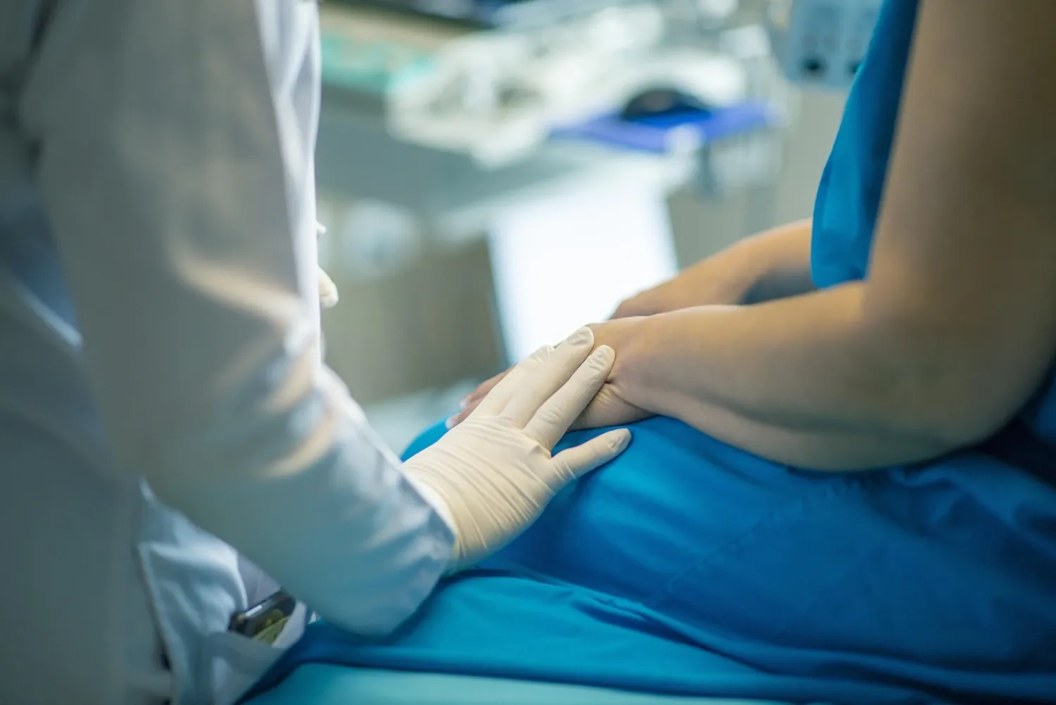 Närbild på två sittande människor, snett bakifrån. En sjuksköterska lägger sin hand på patientens arm.