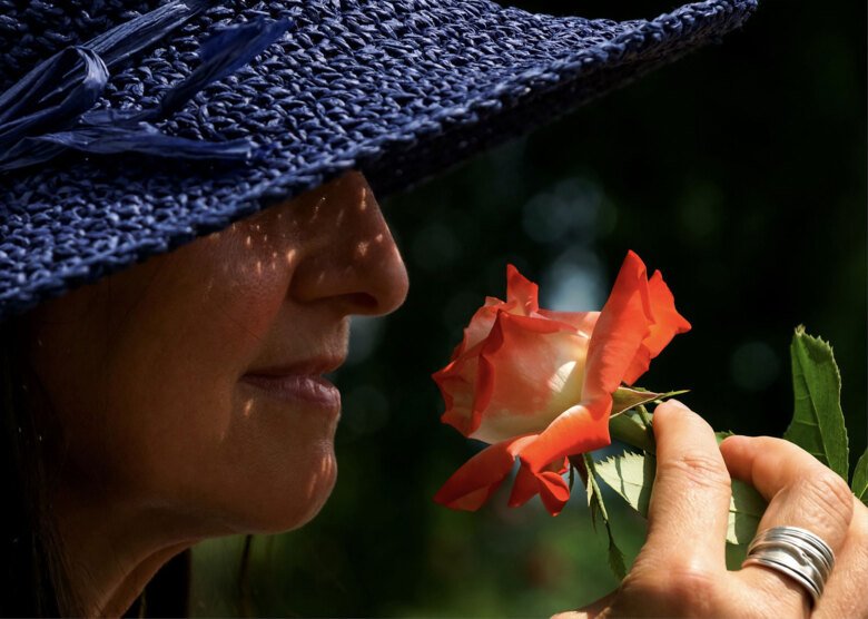 kvinna i profil, under hatt som luktar på en blomma.
