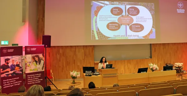 Lektor Lisette Farias Vera föreläser om vad arbetsterapi är och vad hennes forskning handlar om. Hon står framme vid podiet med en Powerpoint på skärmen.