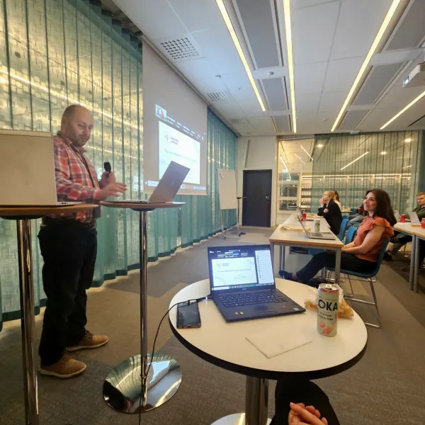 Foto på Mark Issa som står längst framme i ett större mötesrum med mikrofon i handen.