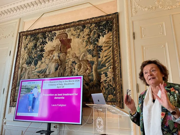 Laura Fratiglioni föreläser på italienska ambassaden. Hon står vid ett litet podium och skärm syns.