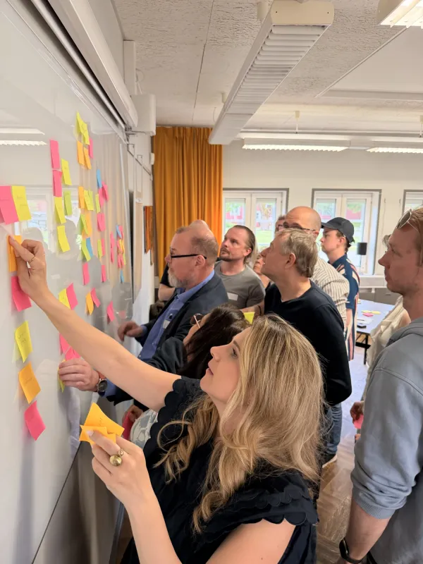 Bild på personer som samarbetar och sätter post-its på en whiteboard tavla.