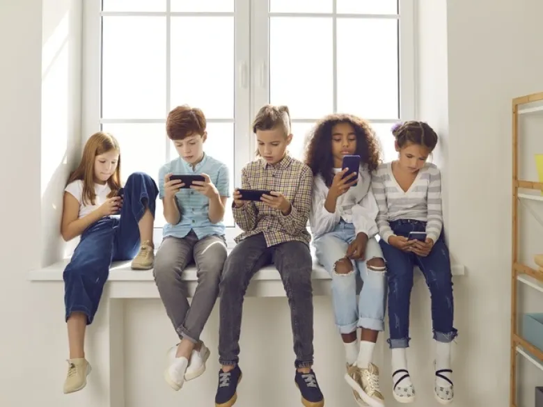 Barn som sitter bredvid varandra och tittar på sina mobiltelefoner