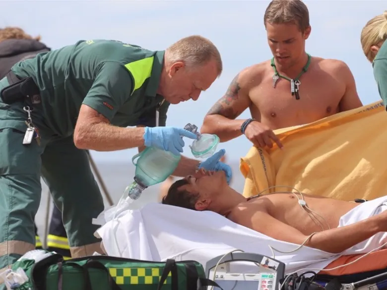 Ambulanspersonal och andra tar hand om en drunknad som ligger på en bår.
