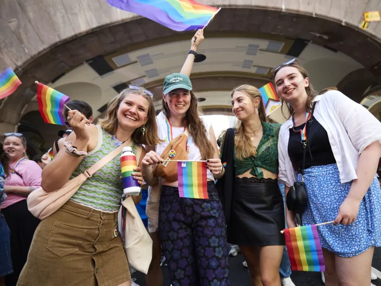 Alina Lapp, Maureen Verdier, Teresa Reindl och Katharina Schormair under paraden på gatan och håller i regnbågsflagor och ler.