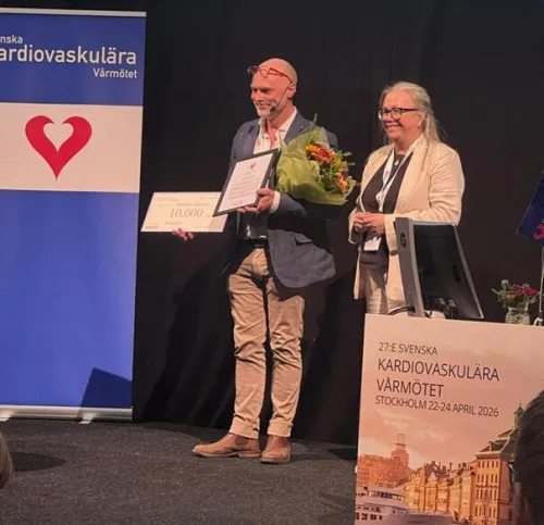 Andreas on a stage with a fram prize and flowers.
