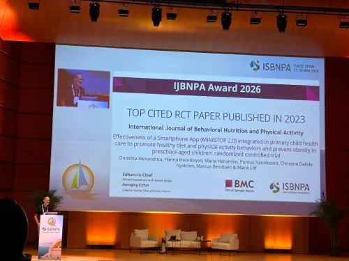 A stage with a large screen displaying the winners of the Best Cited RCT Award, 2023. A man is standing behind a lectern on the stage.