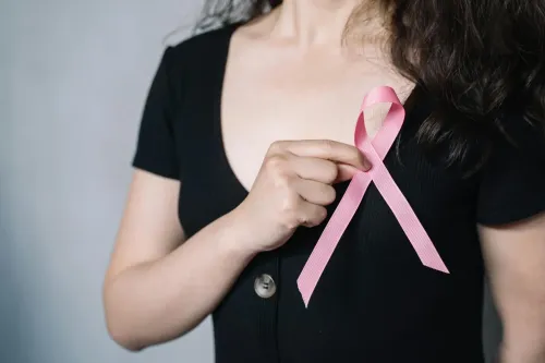 Woman holding a pink ribbon in front of her chest.