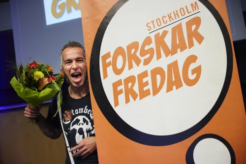 Erik Andersson next to a sign for Forskar Fredag with a bouqet of flowers