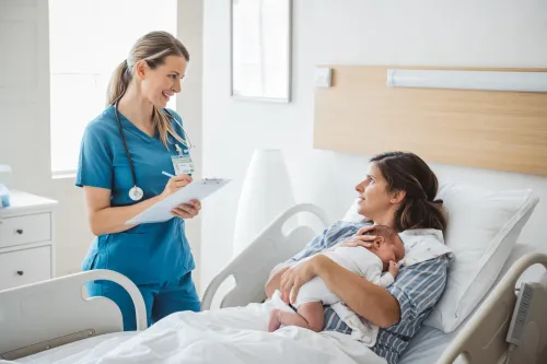 Nurse taking personal data from mother and talking to her. Mother holding newborn baby.