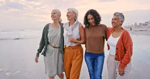 Four happy, laughing middle-aged women stand and hold each other on a beach
