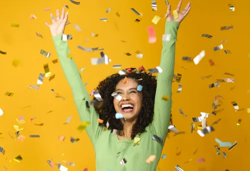 Happy girl with arms in the air surrounded by confetti.