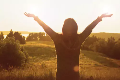 Woman greeting the sun with open arms.