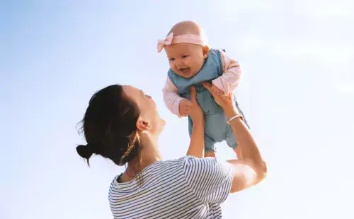 Mother holding baby girl over her head.