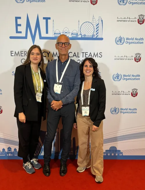 Three people, a man and two women, standing infront of a screen with the WHO&#039;s logo