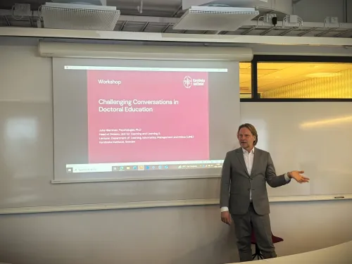 Juha Nieminen in front of a screen with the text Challenging conversations in doctoral education.