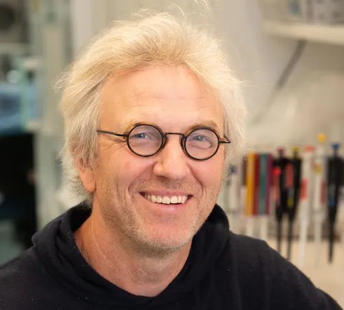 A portrait of a smiling man. He is wearing glasses and a black sweatshirt.