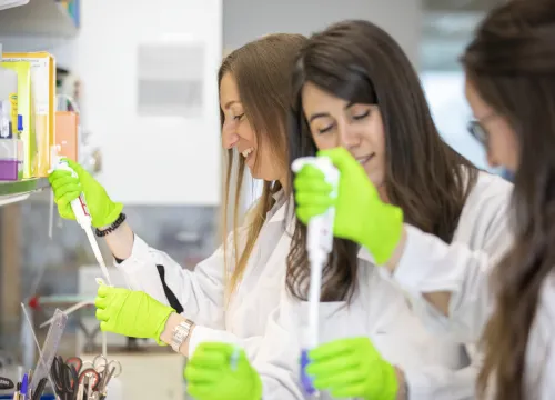 Three female researchers standing with test tubes and pippettes in lab environment.