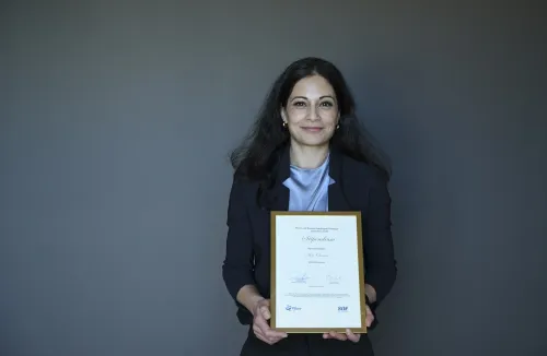 Dark-haired woman holding a diploma in a golden frame.