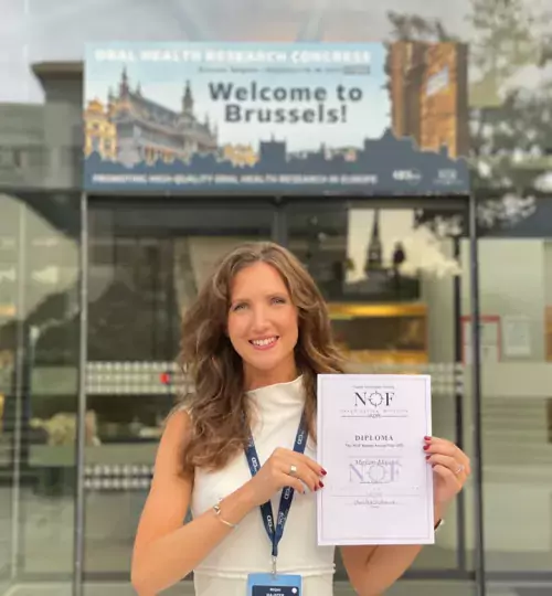 Smiling young woman with a diploma in her hands, in front of a congress building in Brussels.