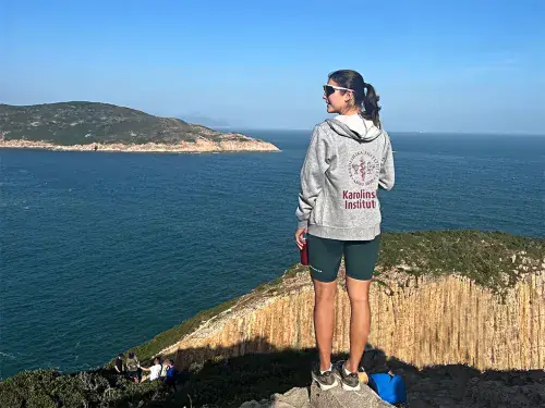 Woman in a KI hoodie standing on a mountain looking at the water