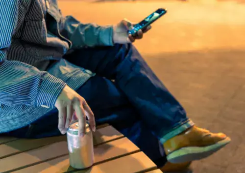 a person on a bench with a drink and a mobile phone